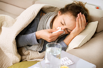 woman on couch blowing nose into tissue